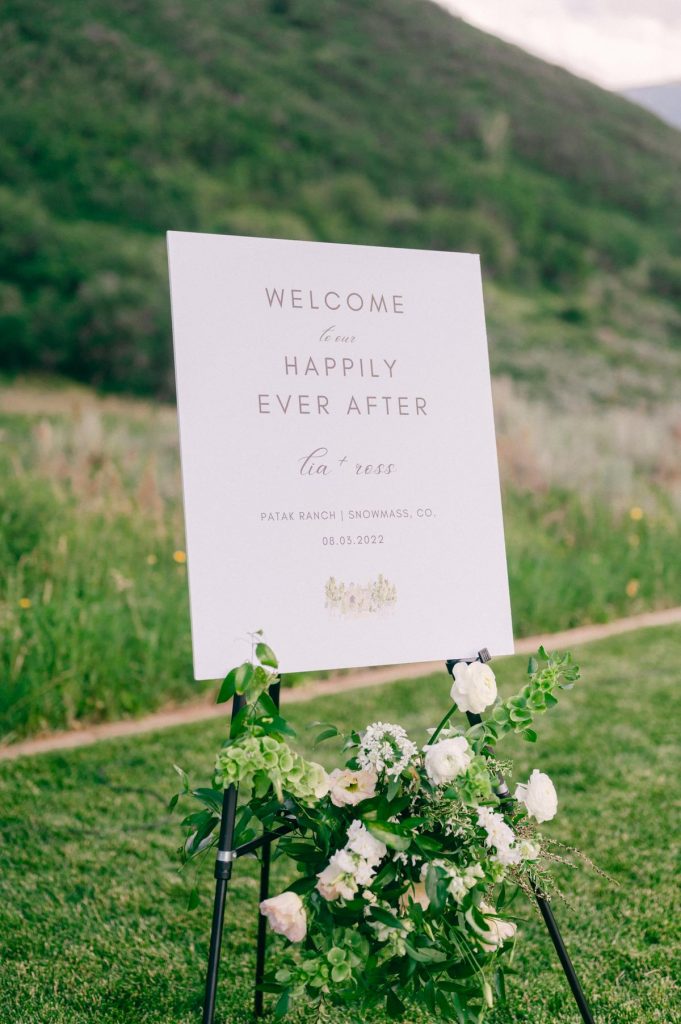 sign on an easel that says "welcome to our happily ever after lie and ross" with a watercolor venue portrait