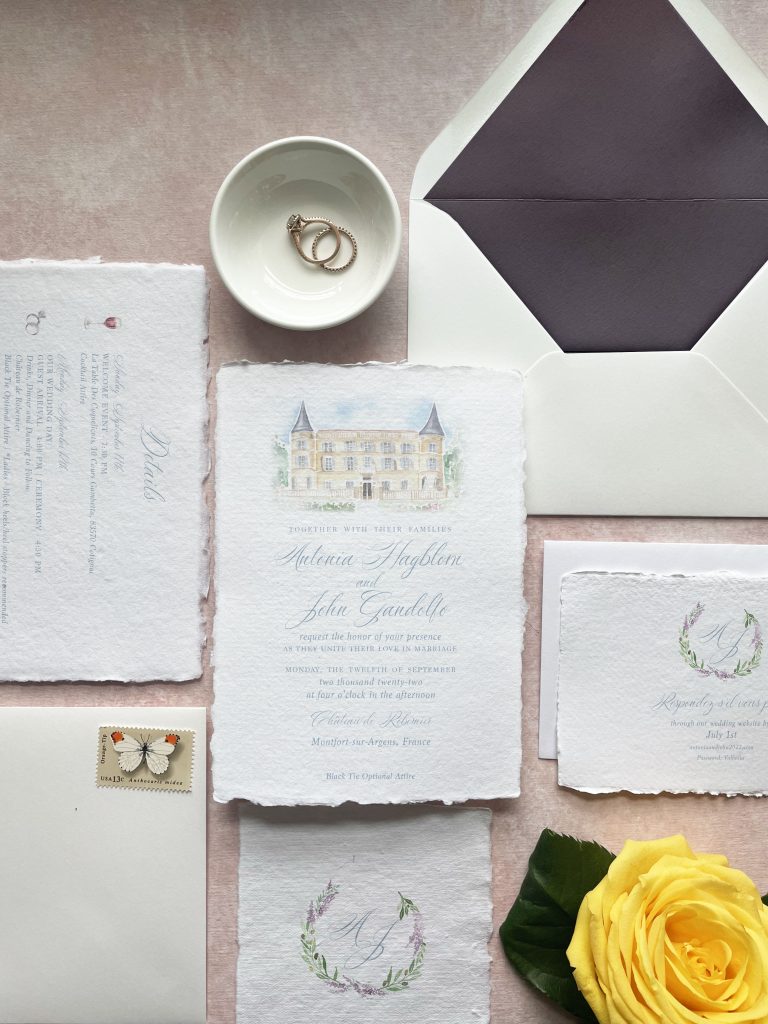 dusty blue wedding invitations with custom watercolor crest and french castle on a pink background